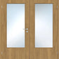 A pair of double interior doors with light oak wood grain and rectangular frosted glass panels, featuring a silver metal lever handle and lock on the left door.