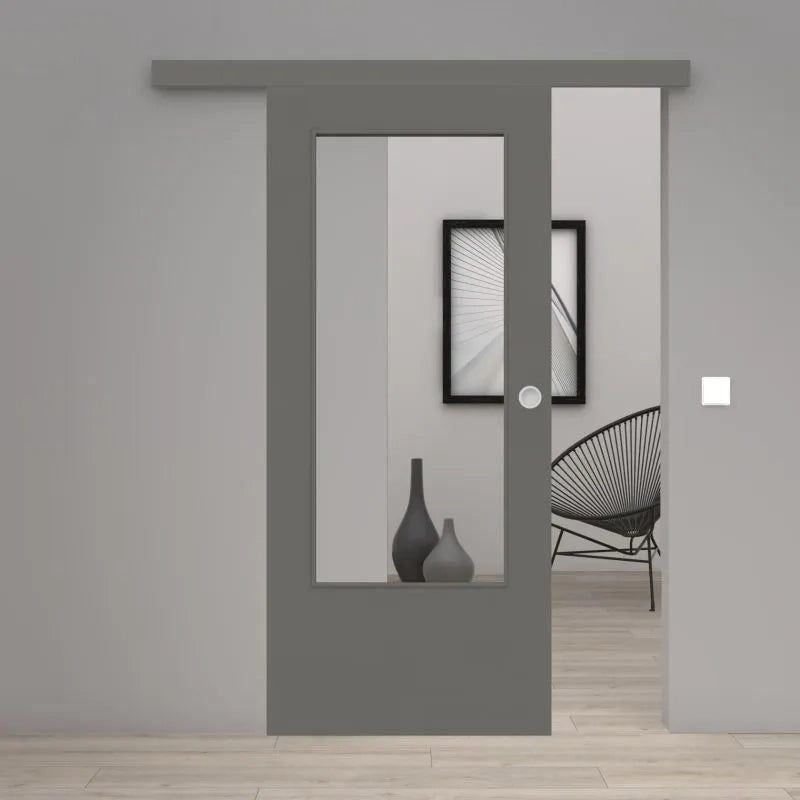 A modern gray sliding door with a large vertical glass panel, shown partially open in a minimalist gray interior room with light wood flooring and a black wire chair.