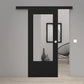 A modern black sliding door with a large vertical glass panel, shown partially open in a minimalist interior setting with light gray walls and light wood flooring.