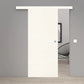 A modern white sliding door with a matching white top rail installed in a gray interior wall, with a black wire chair and light wood floor visible through the opening.