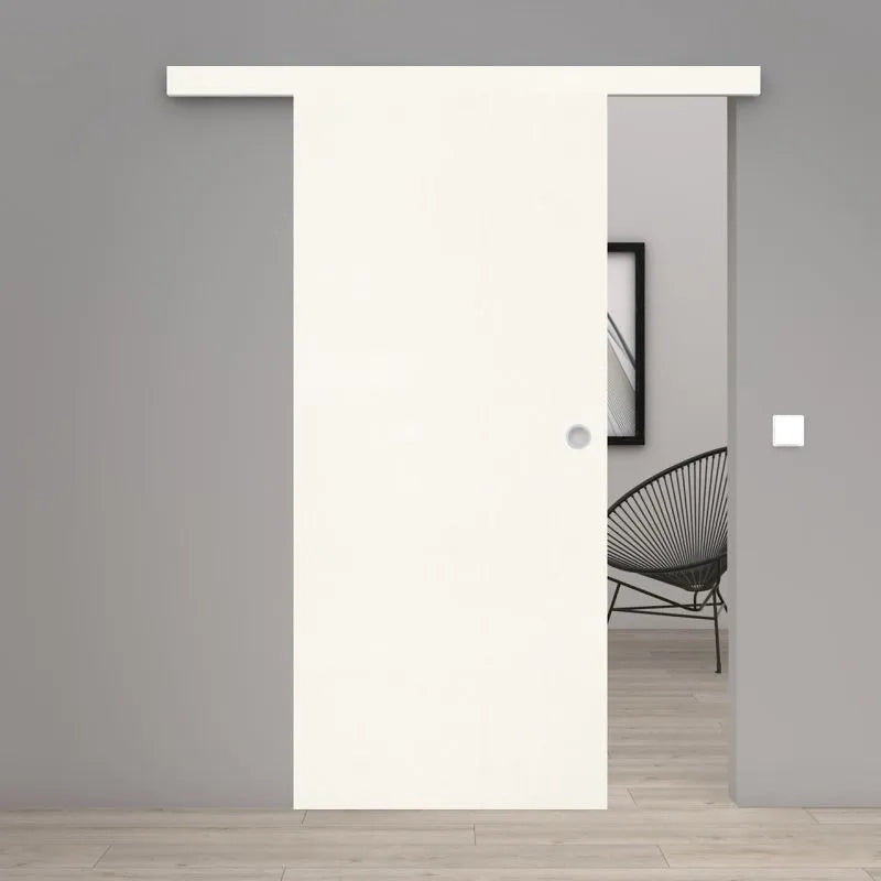 A modern white sliding door with a matching white top rail installed in a gray interior wall, with a black wire chair and light wood floor visible through the opening.