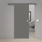 A modern minimalist interior showing a matte gray sliding door with a matching top rail and a small round silver handle. The door is slightly open, revealing a glimpse of a black wire chair and framed wall art in the background room, set against light gray walls and light wood flooring.