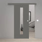 A modern gray sliding door with a vertical rectangular glass panel, shown installed in a minimalist interior setting with light wood flooring and neutral walls.