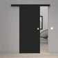 A modern black sliding door with a minimalist design, shown partially open in a contemporary room with light gray walls and light wood flooring.
