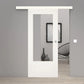 A modern white sliding door with a large rectangular glass panel, shown installed in a minimalist gray interior room with light wood flooring and a black wire chair.