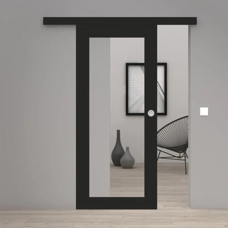A modern black sliding door with a large vertical glass panel and a small round white doorknob, shown installed in a minimalist gray interior room with light wood flooring.