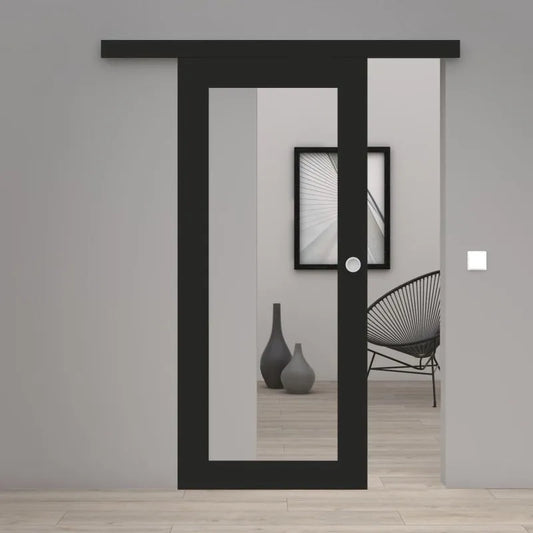 A modern black sliding door with a large vertical glass panel and a small round white doorknob, shown installed in a minimalist gray interior room with light wood flooring.